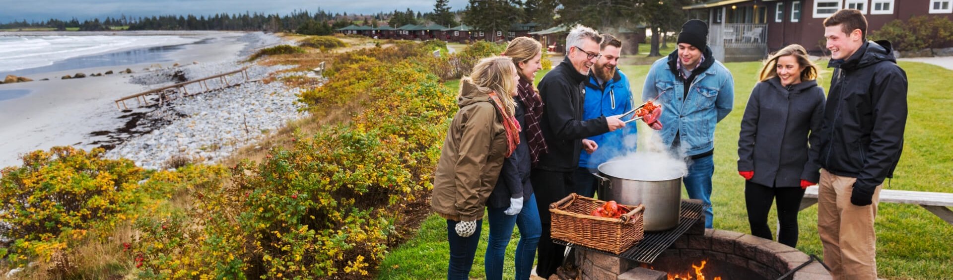 a family boiling lobster on an outdoor fire pit