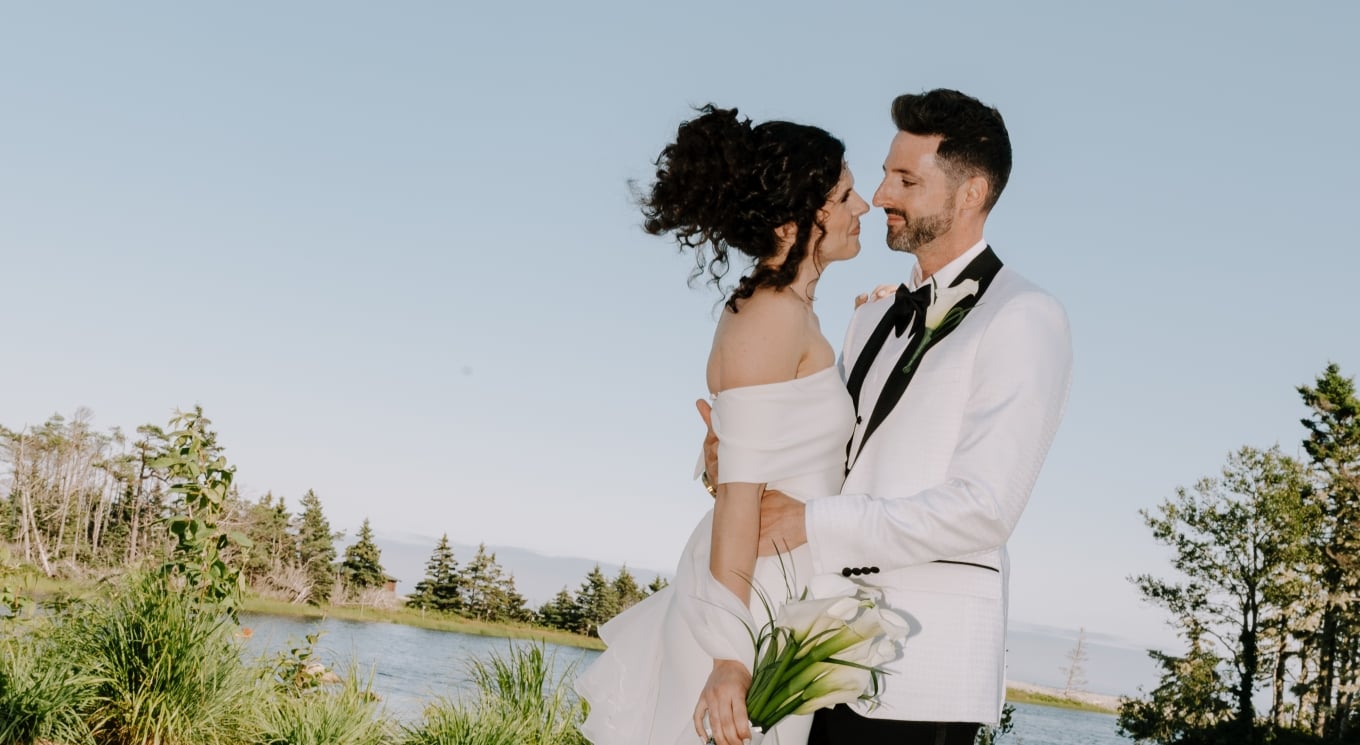 a bride and groom embracing by a lake