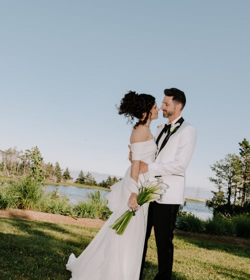 a bride and groom embracing by a lake